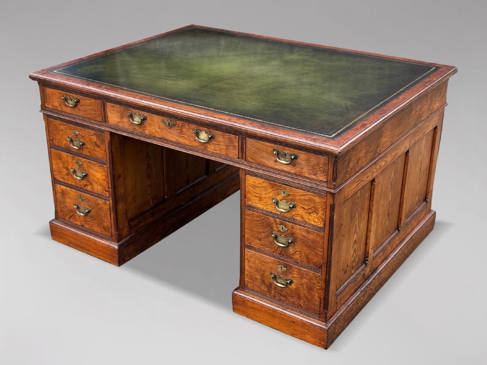 A Victorian pitch pine partners desk featuring a green leather inset writing surface, twin pedestals, and brass swan-neck handles.