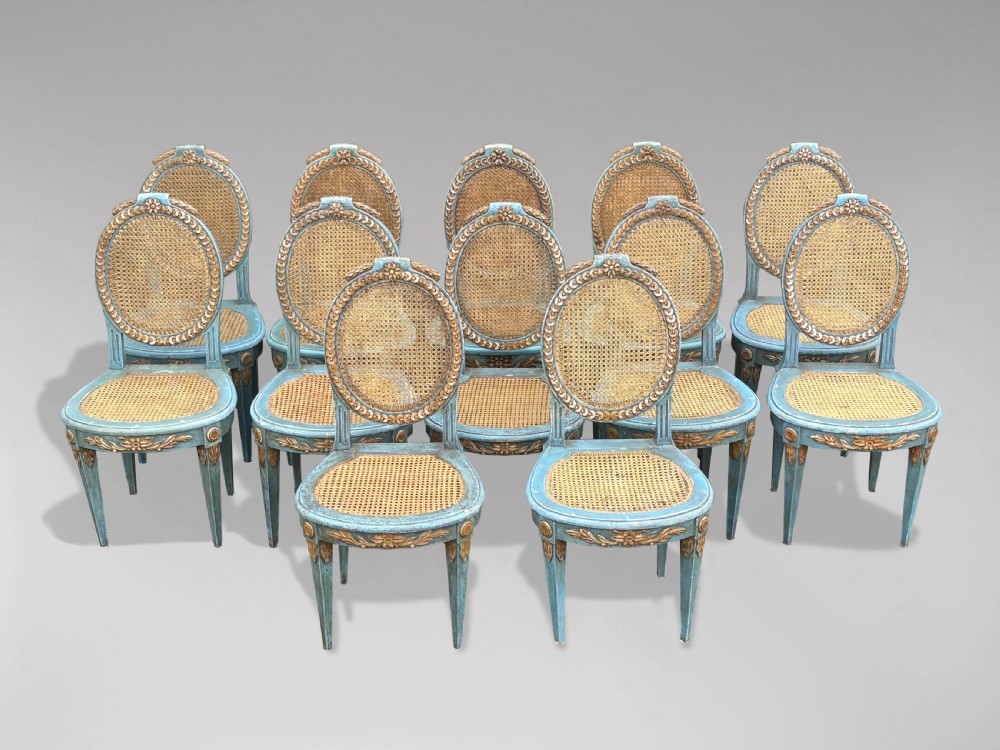 A set of twelve French Louis XVI style dining chairs with blue painted and gilded frames, oval cane backs, and cane seats.