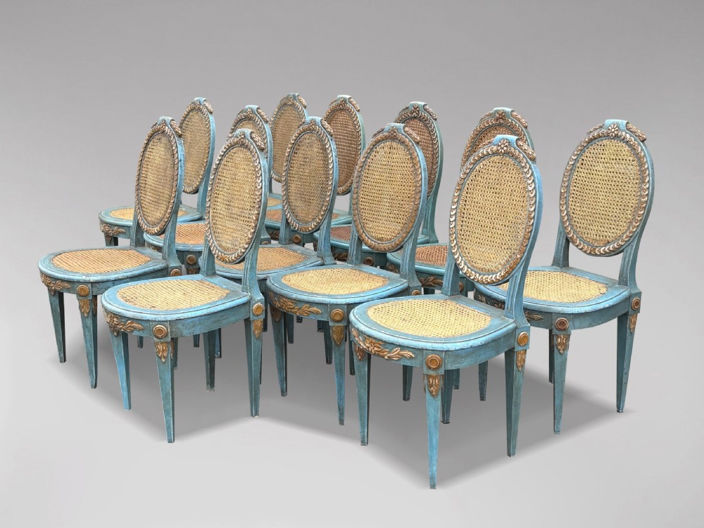 A set of twelve French Louis XVI style dining chairs with blue painted and gilded frames, oval cane backs, and cane seats. View II