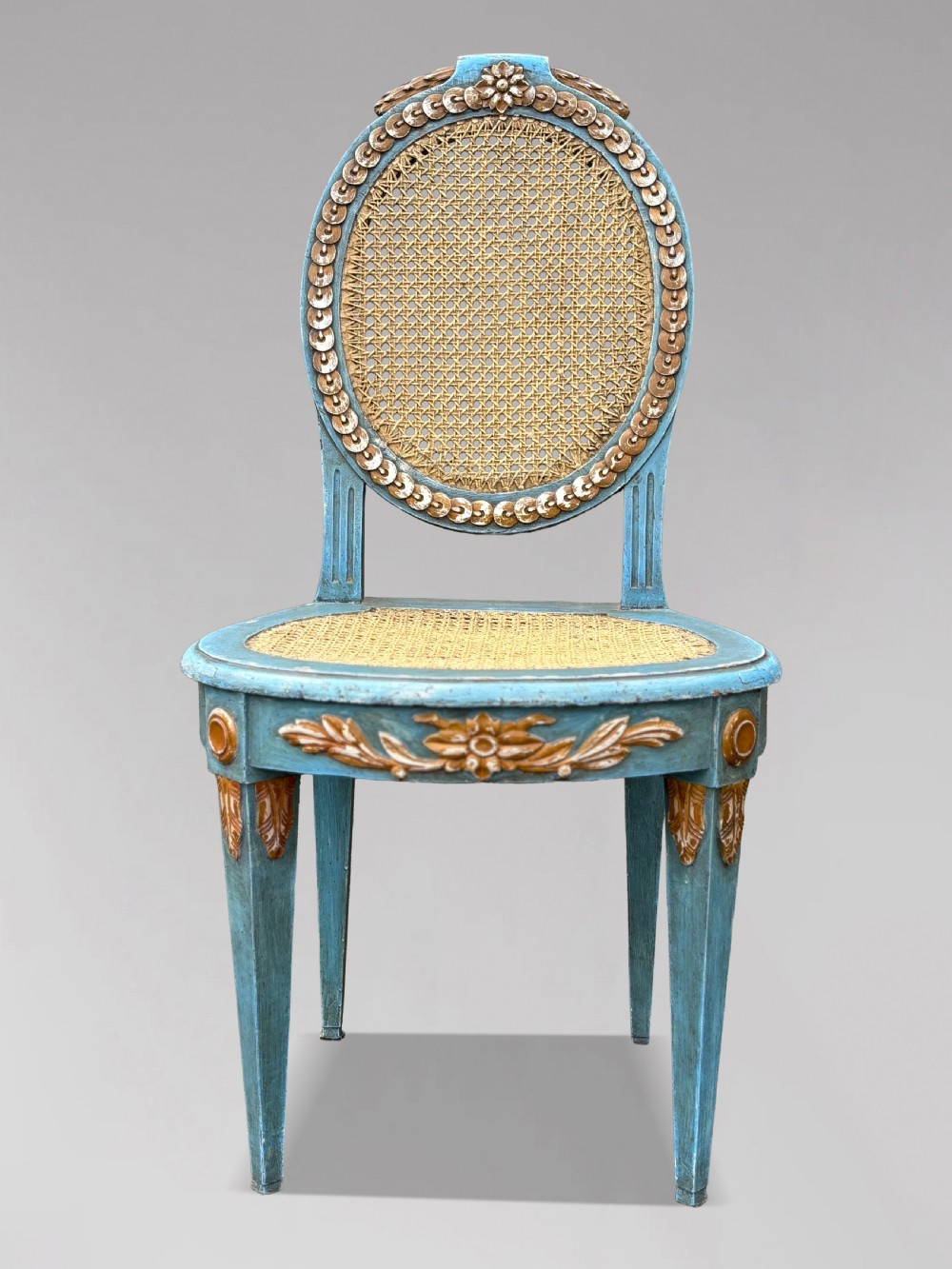 A set of twelve French Louis XVI style dining chairs with blue painted and gilded frames, oval cane backs, and cane seats. View III