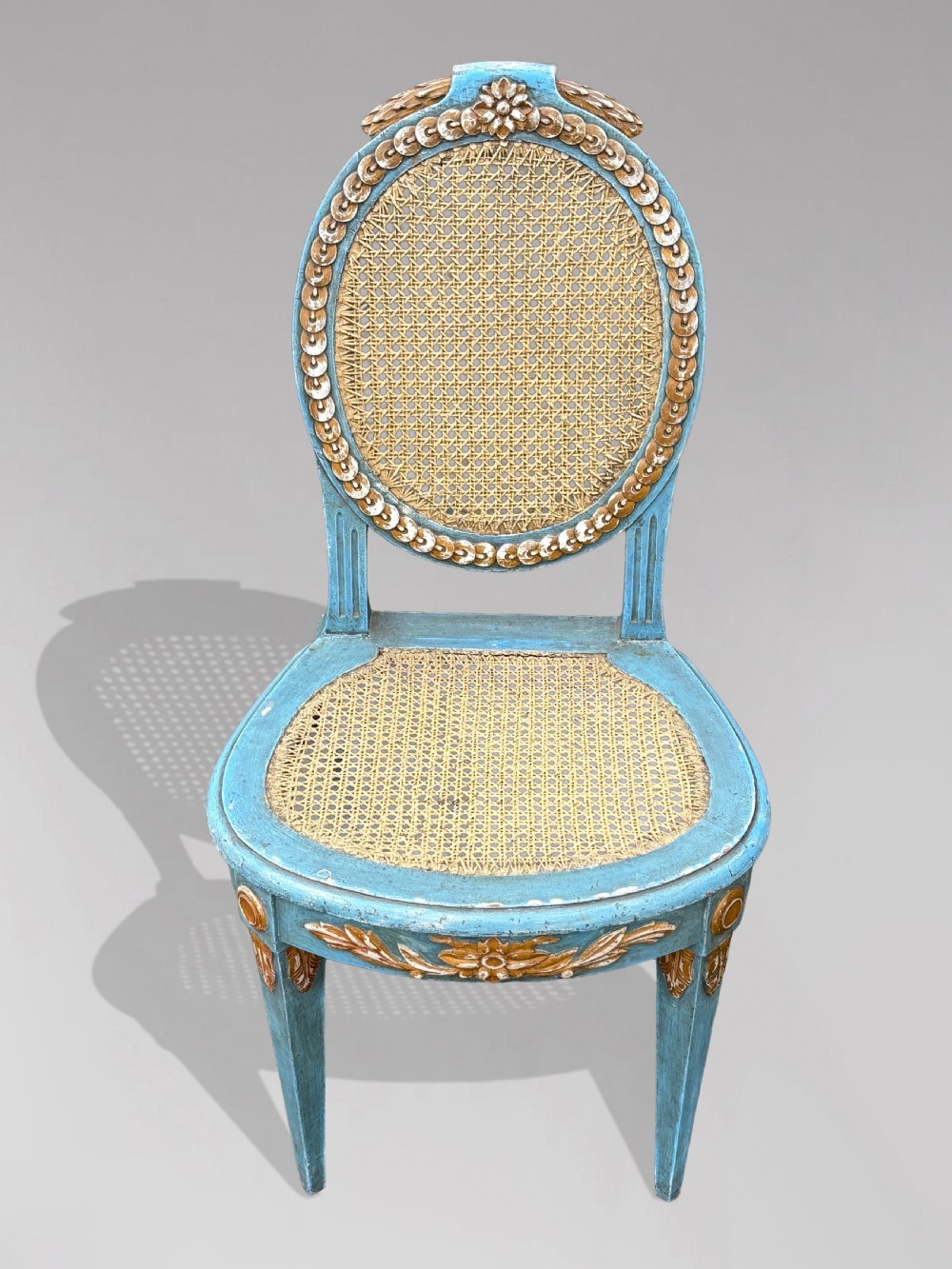 A set of twelve French Louis XVI style dining chairs with blue painted and gilded frames, oval cane backs, and cane seats. View IV