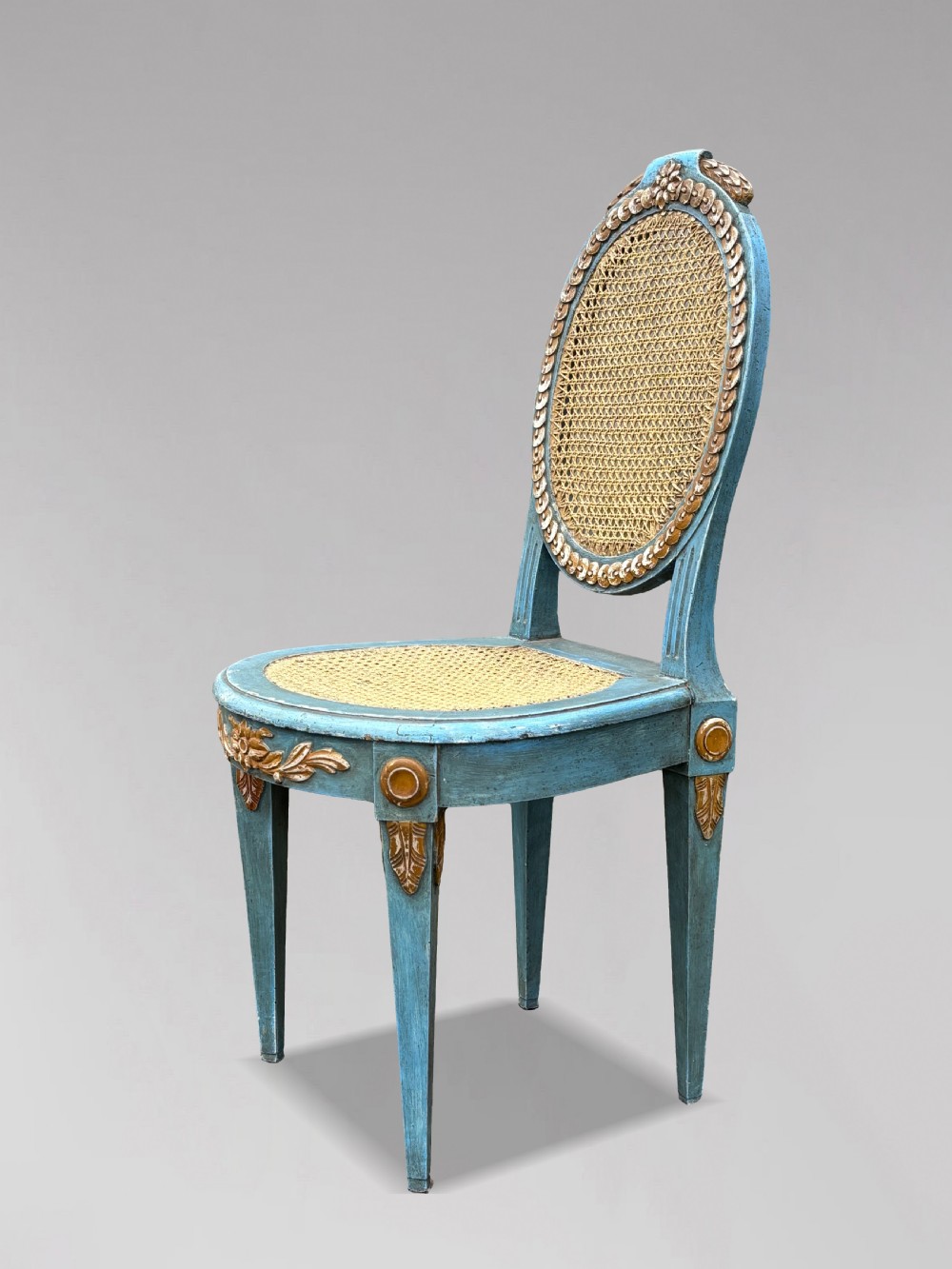 A set of twelve French Louis XVI style dining chairs with blue painted and gilded frames, oval cane backs, and cane seats. View V