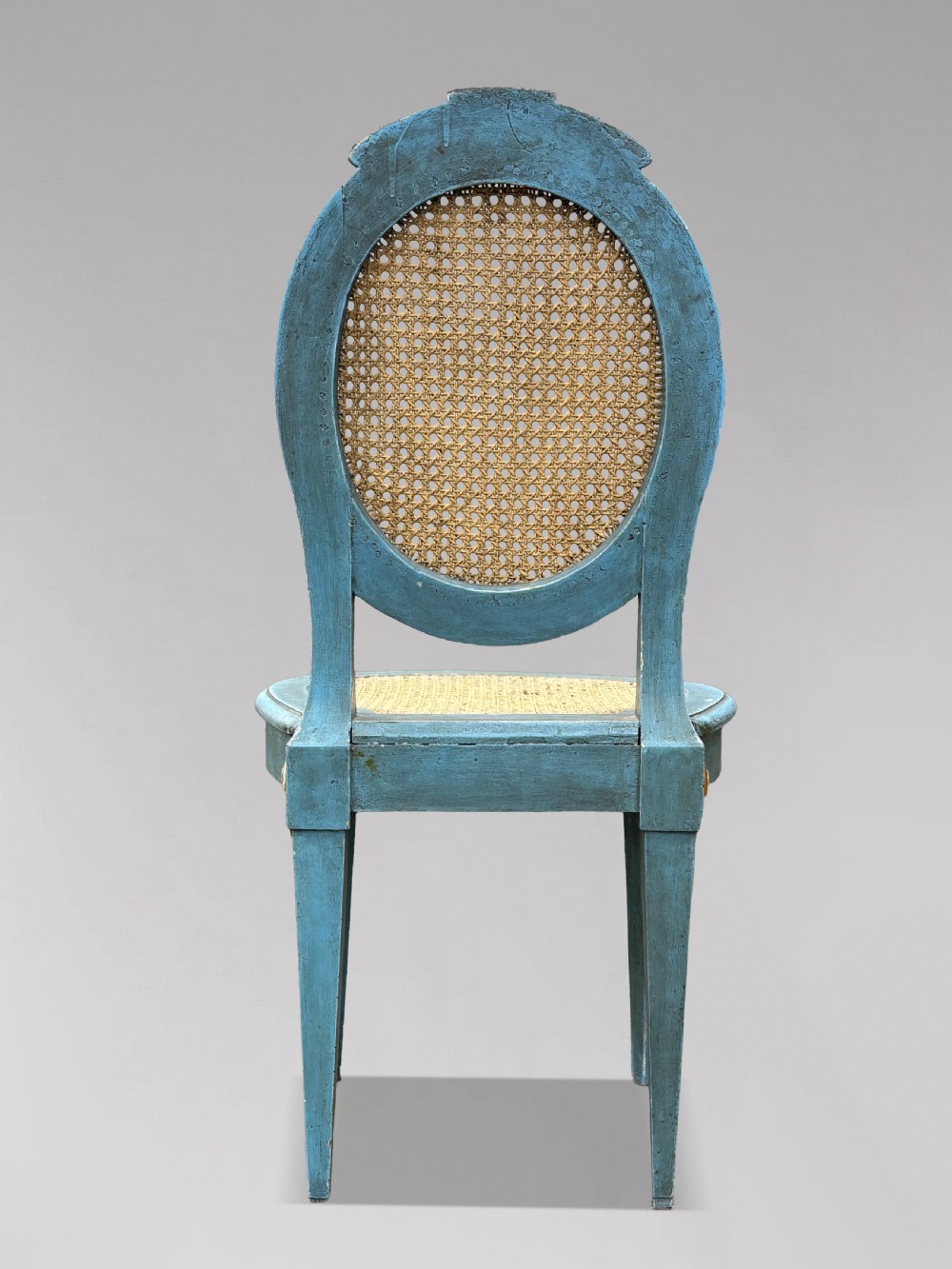 A set of twelve French Louis XVI style dining chairs with blue painted and gilded frames, oval cane backs, and cane seats. View VI
