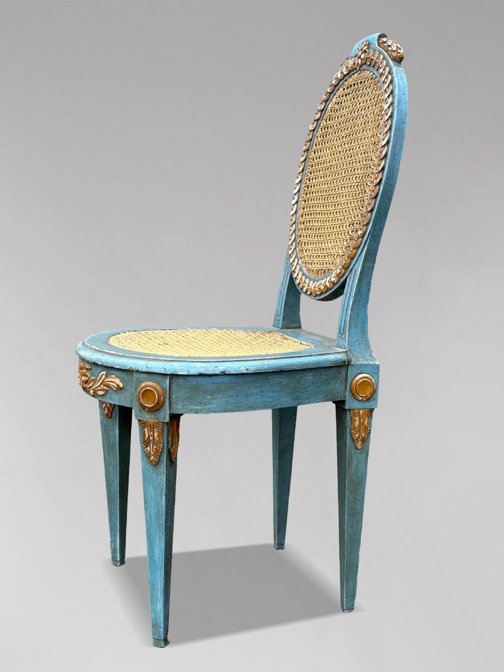 A set of twelve French Louis XVI style dining chairs with blue painted and gilded frames, oval cane backs, and cane seats. View VII