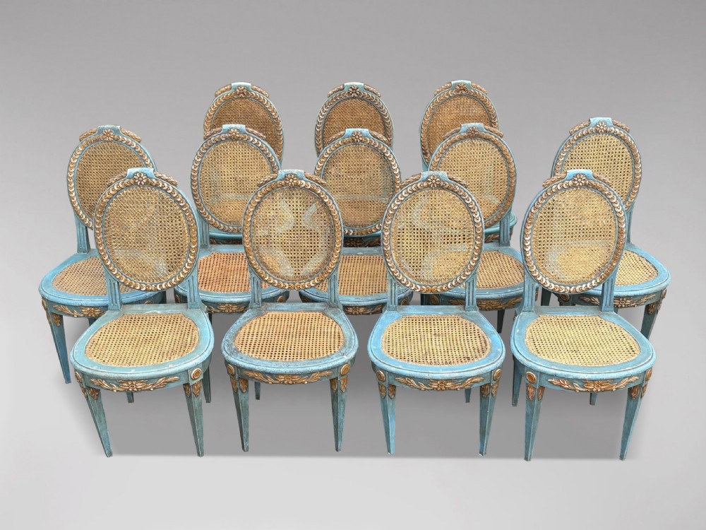 A set of twelve French Louis XVI style dining chairs with blue painted and gilded frames, oval cane backs, and cane seats. View VIII