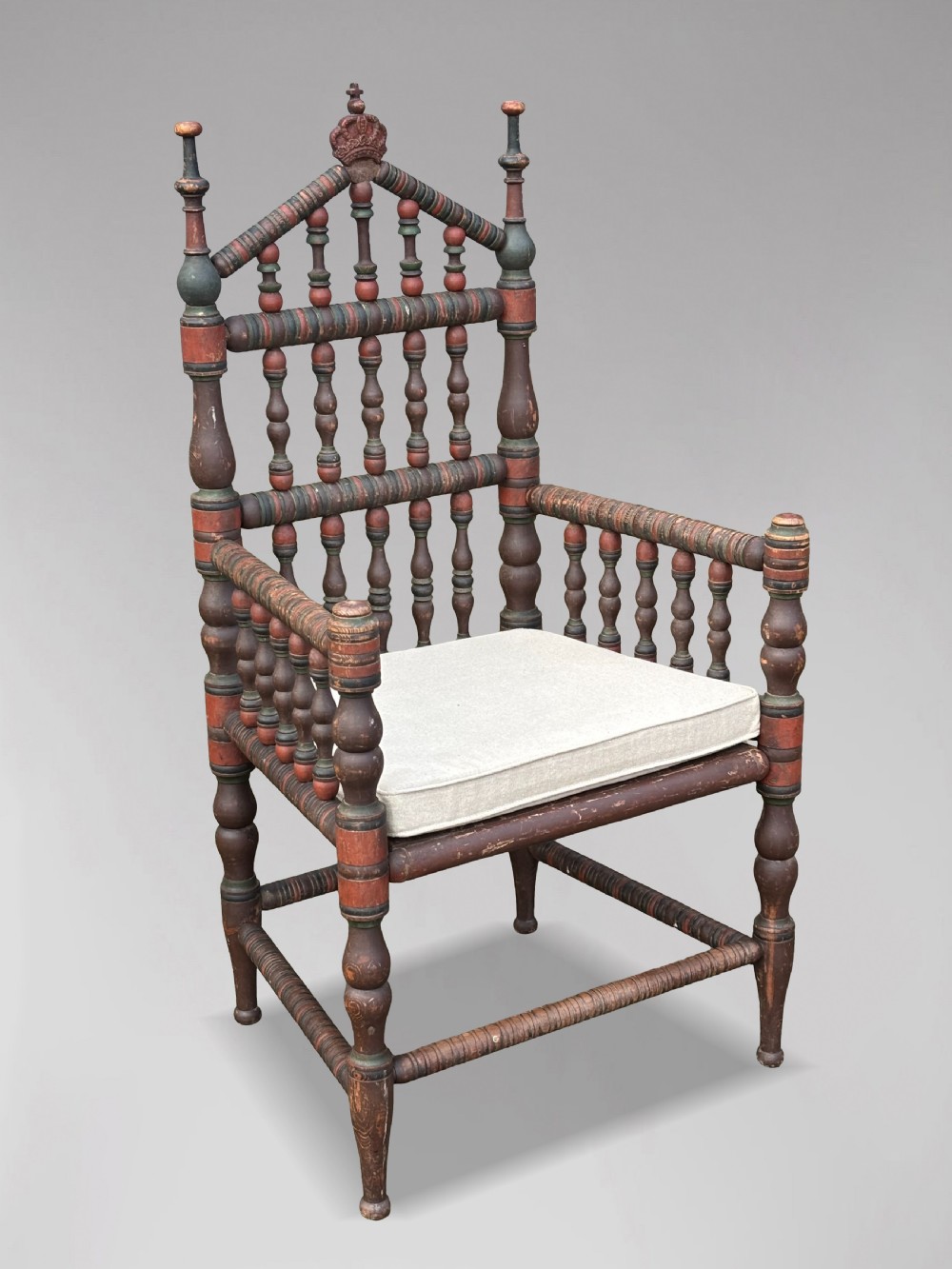 A 19th-century Swedish country throne armchair constructed with polychrome turned bobbins, a carved crown top finial, and a light cushion.