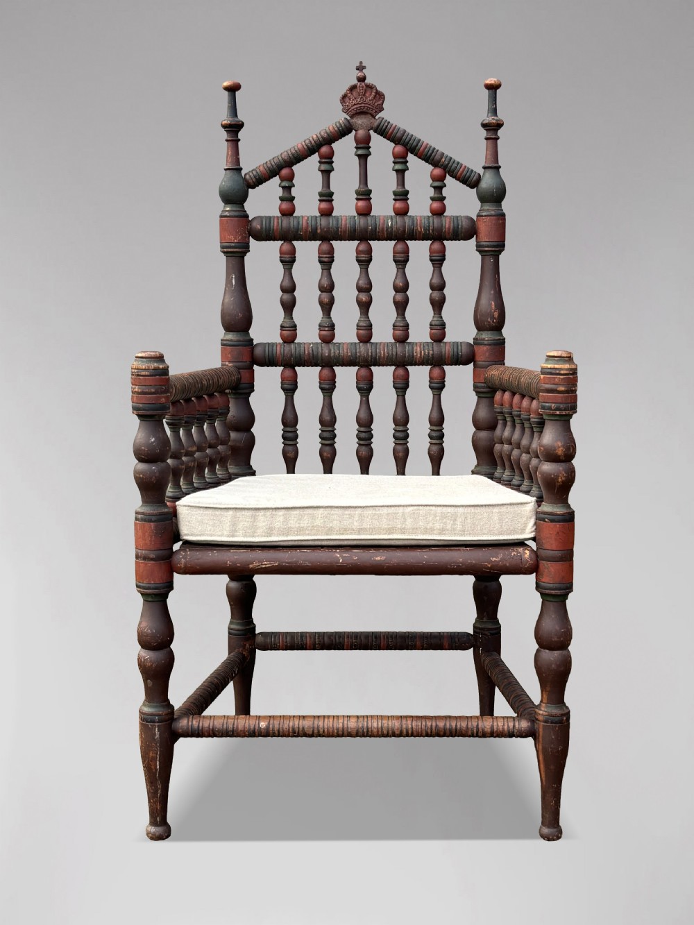 A 19th-century Swedish country throne armchair constructed with polychrome turned bobbins, a carved crown top finial, and a light cushion. View II