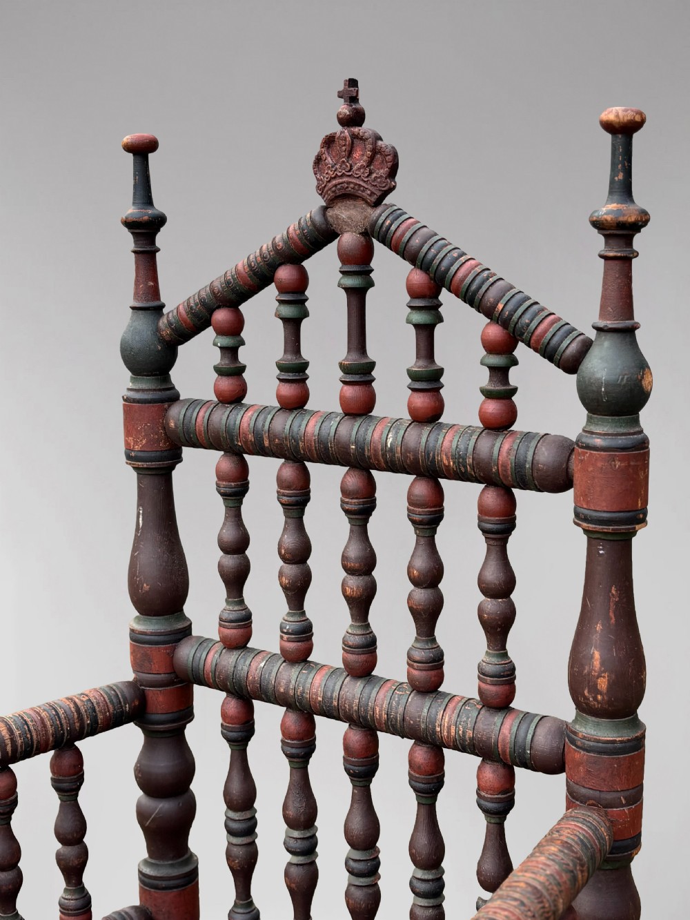 A 19th-century Swedish country throne armchair constructed with polychrome turned bobbins, a carved crown top finial, and a light cushion. View V