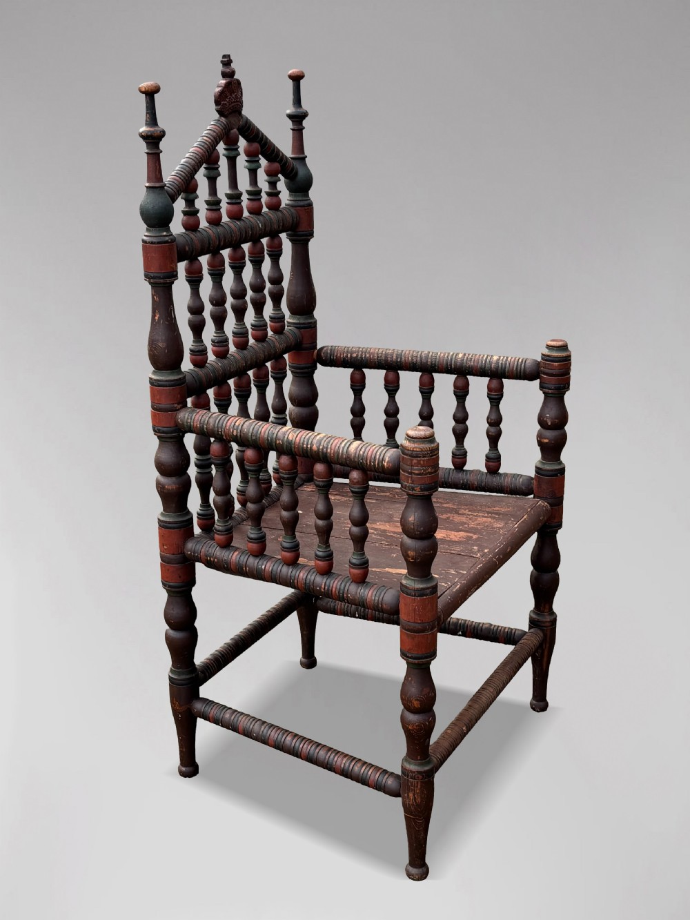 A 19th-century Swedish country throne armchair constructed with polychrome turned bobbins, a carved crown top finial, and a light cushion. View X