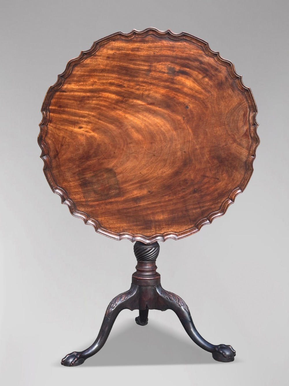 An 18th-century George III mahogany tilt-top tripod table featuring a carved piecrust rim, a fluted column, and cabriole legs ending in claw and ball feet.