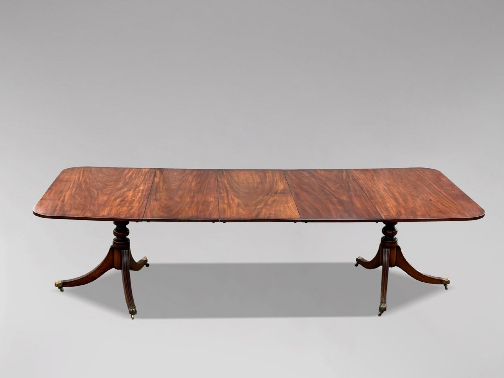 An early nineteenth-century mahogany twin pedestal dining table with a rounded rectangular top, reeded splayed legs, and brass castors.