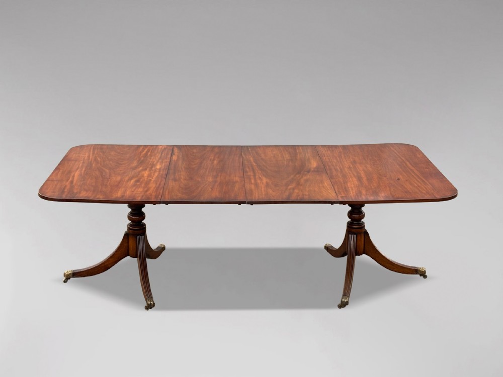 An early nineteenth-century mahogany twin pedestal dining table with a rounded rectangular top, reeded splayed legs, and brass castors. View II