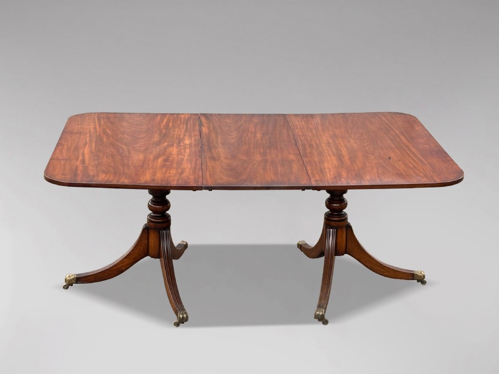 An early nineteenth-century mahogany twin pedestal dining table with a rounded rectangular top, reeded splayed legs, and brass castors. View III