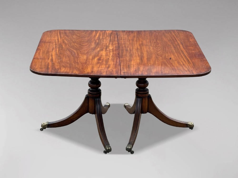 An early nineteenth-century mahogany twin pedestal dining table with a rounded rectangular top, reeded splayed legs, and brass castors. View V