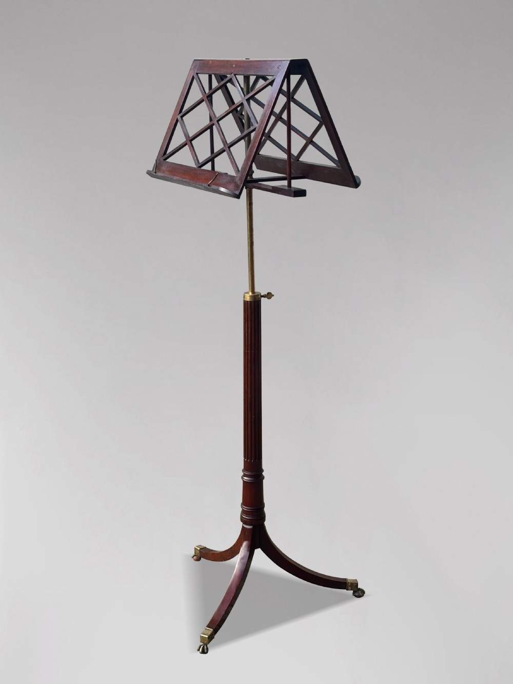 A 19th-century Regency mahogany duet music stand featuring a double-sided lattice desk, adjustable brass column, fluted stem, and tripod base with brass castors.