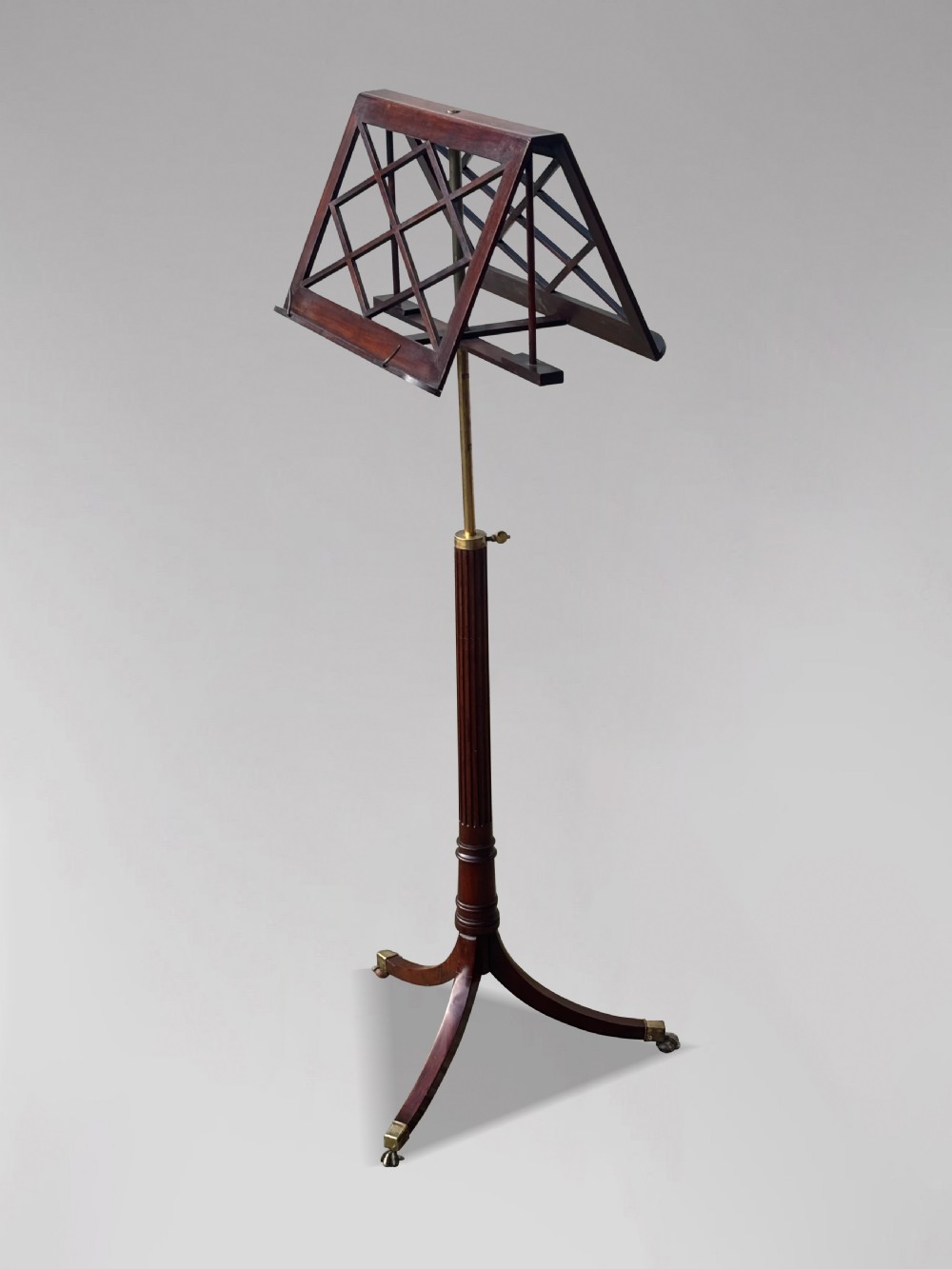 A 19th-century Regency mahogany duet music stand featuring a double-sided lattice desk, adjustable brass column, fluted stem, and tripod base with brass castors. View VIII