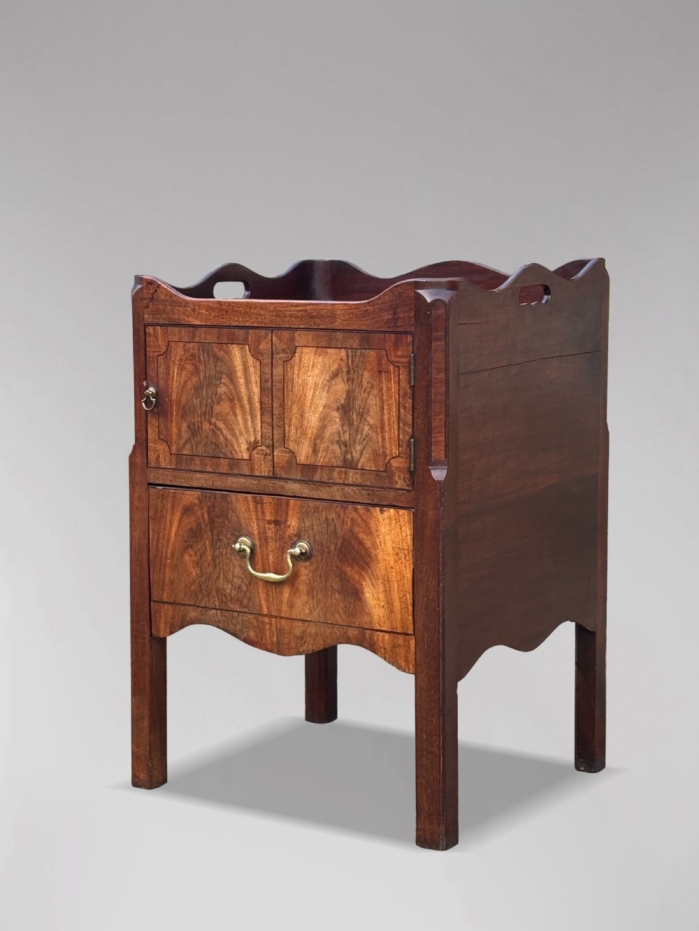 An 18th-century George III mahogany tray-top commode featuring shaped gallery sides, a cupboard with twin panel doors, a lower drawer with brass swan-neck handle, and square legs.