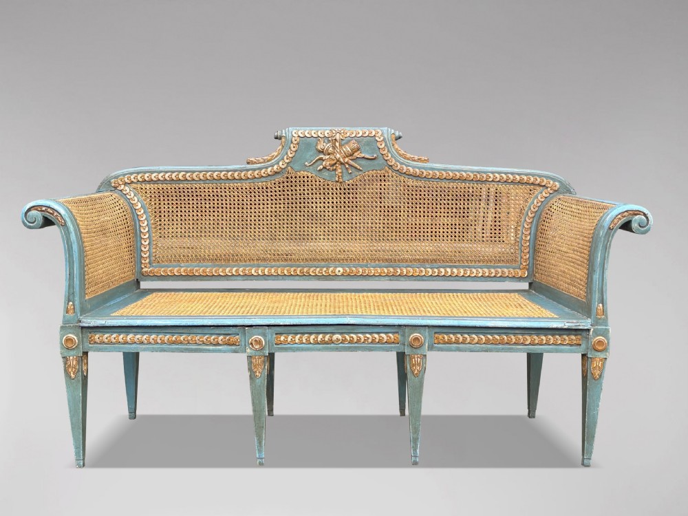 A late 19th-century Louis XVI style settee featuring blue painted trim with gold leaf details, woven cane seat and back panels, and six fluted legs.
