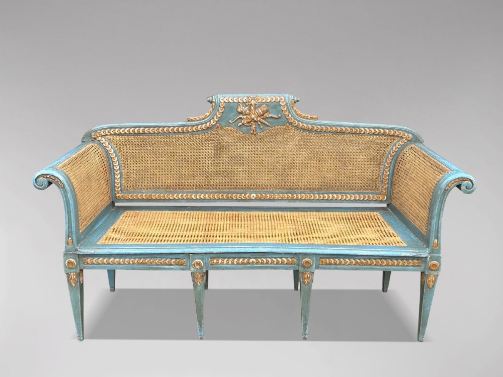 A late 19th-century Louis XVI style settee featuring blue painted trim with gold leaf details, woven cane seat and back panels, and six fluted legs. View II
