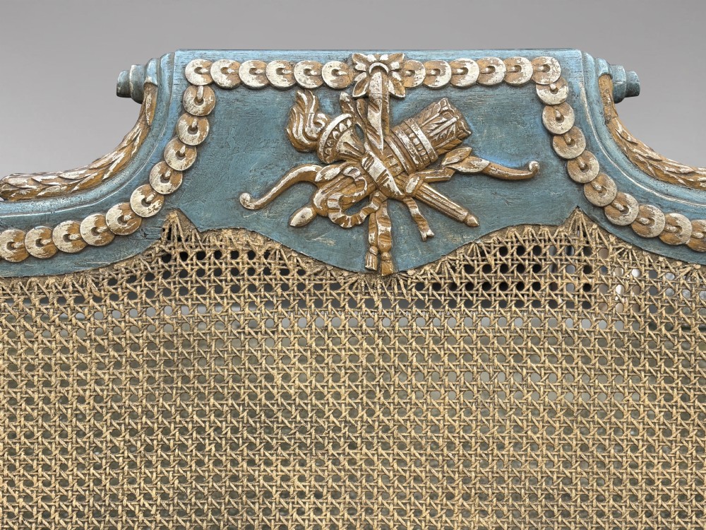 A late 19th-century Louis XVI style settee featuring blue painted trim with gold leaf details, woven cane seat and back panels, and six fluted legs. View IV