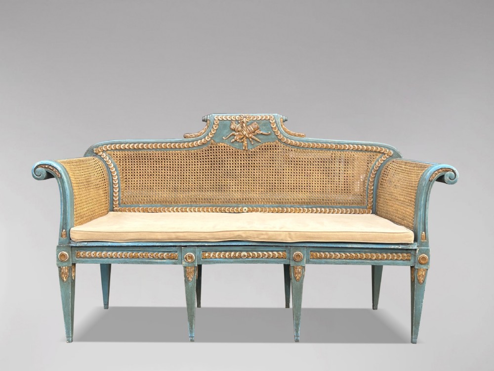 A late 19th-century Louis XVI style settee featuring blue painted trim with gold leaf details, woven cane seat and back panels, and six fluted legs. View V