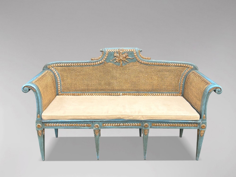 A late 19th-century Louis XVI style settee featuring blue painted trim with gold leaf details, woven cane seat and back panels, and six fluted legs. View VI