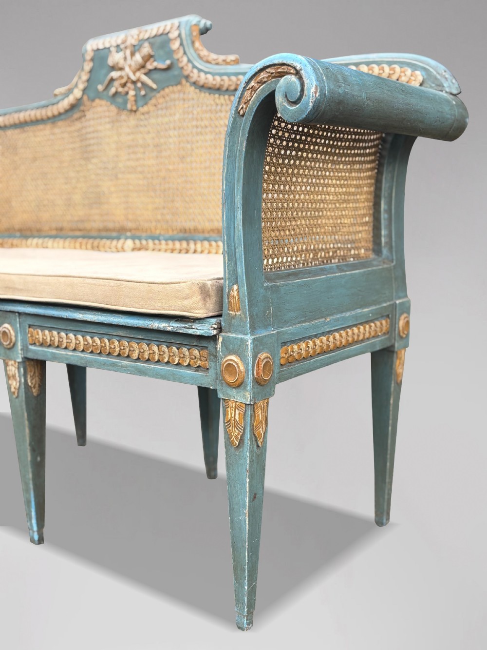 A late 19th-century Louis XVI style settee featuring blue painted trim with gold leaf details, woven cane seat and back panels, and six fluted legs. View VII
