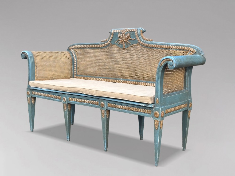 A late 19th-century Louis XVI style settee featuring blue painted trim with gold leaf details, woven cane seat and back panels, and six fluted legs. View X