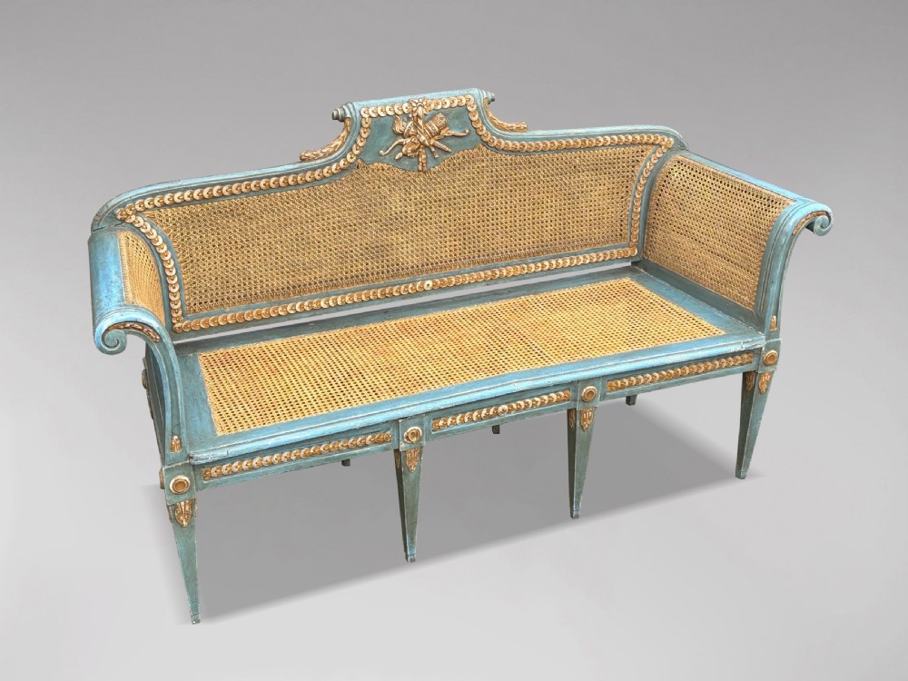 A late 19th-century Louis XVI style settee featuring blue painted trim with gold leaf details, woven cane seat and back panels, and six fluted legs. View XI