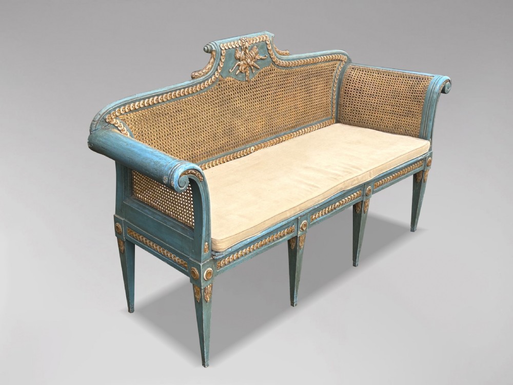 A late 19th-century Louis XVI style settee featuring blue painted trim with gold leaf details, woven cane seat and back panels, and six fluted legs. View XII