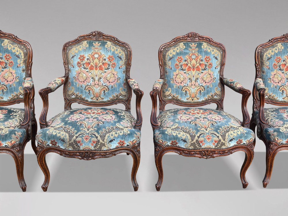 A set of four 19th-century French Louis XV style fauteuil armchairs featuring carved timber frames, cabriole legs, and blue floral upholstery.