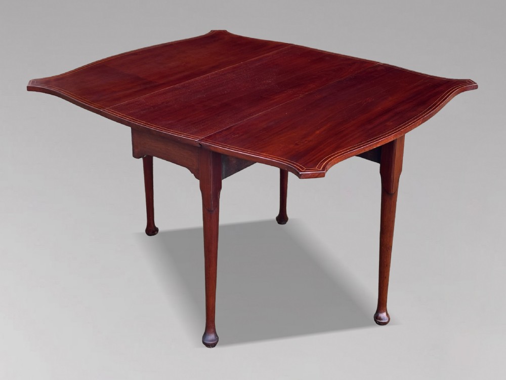 An 18th-century George III mahogany drop-leaf table featuring shaped corner edges with fine stringing inlay and slender legs terminating in pad feet.