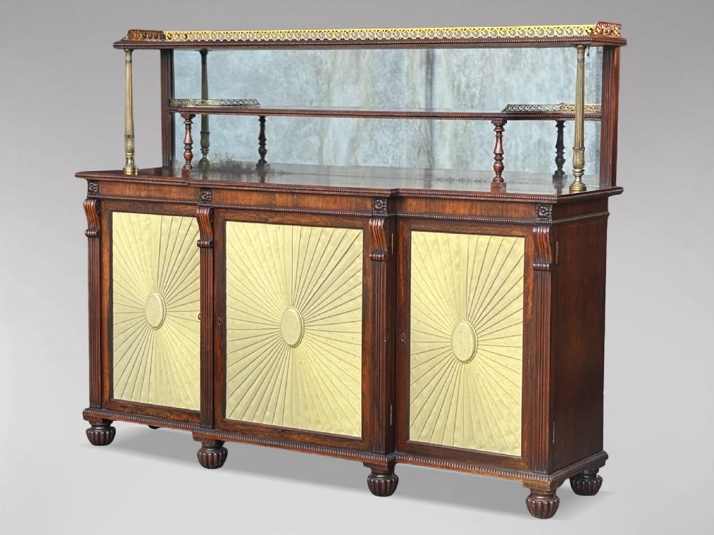 A Regency rosewood sideboard featuring three doors with sunburst pleated panels, a mirrored upper shelf supported by brass columns, and a pierced brass top gallery.