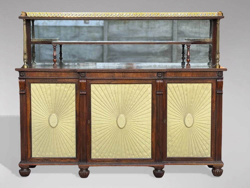 A Regency rosewood sideboard featuring three doors with sunburst pleated panels, a mirrored upper shelf supported by brass columns, and a pierced brass top gallery. View II