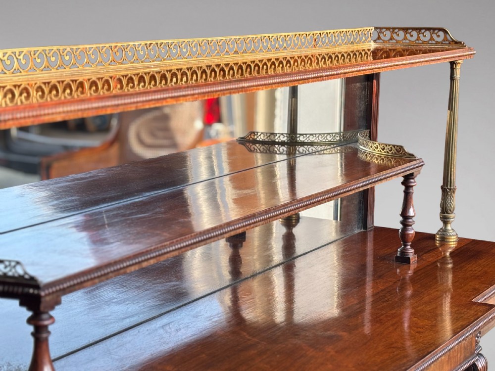 A Regency rosewood sideboard featuring three doors with sunburst pleated panels, a mirrored upper shelf supported by brass columns, and a pierced brass top gallery. View VI