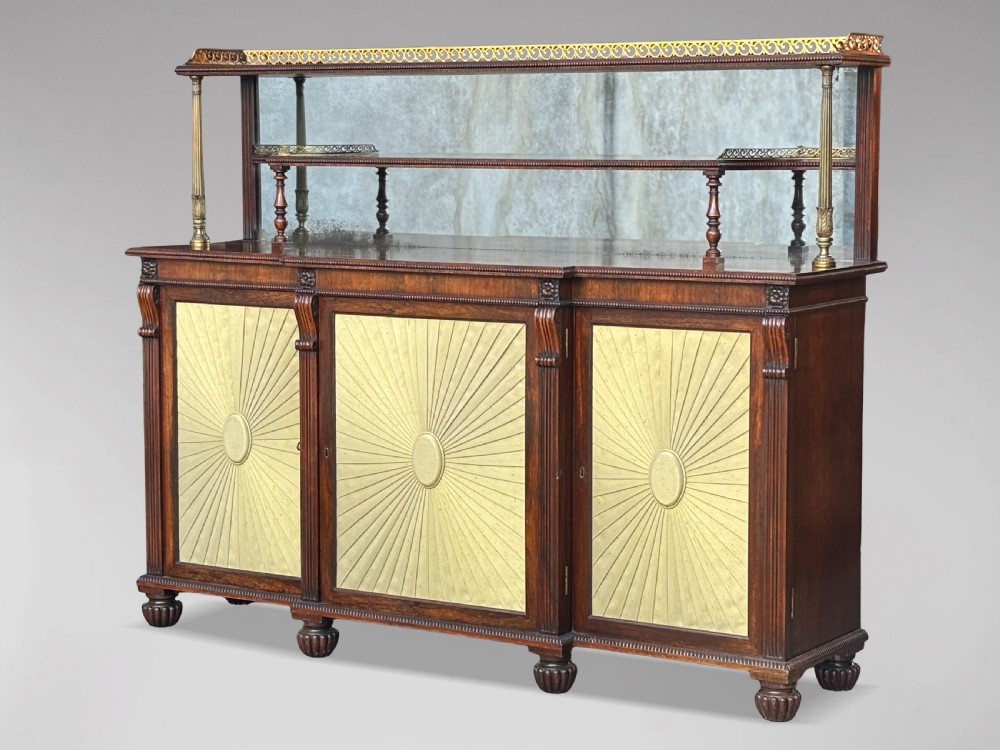 A Regency rosewood sideboard featuring three doors with sunburst pleated panels, a mirrored upper shelf supported by brass columns, and a pierced brass top gallery. View VII