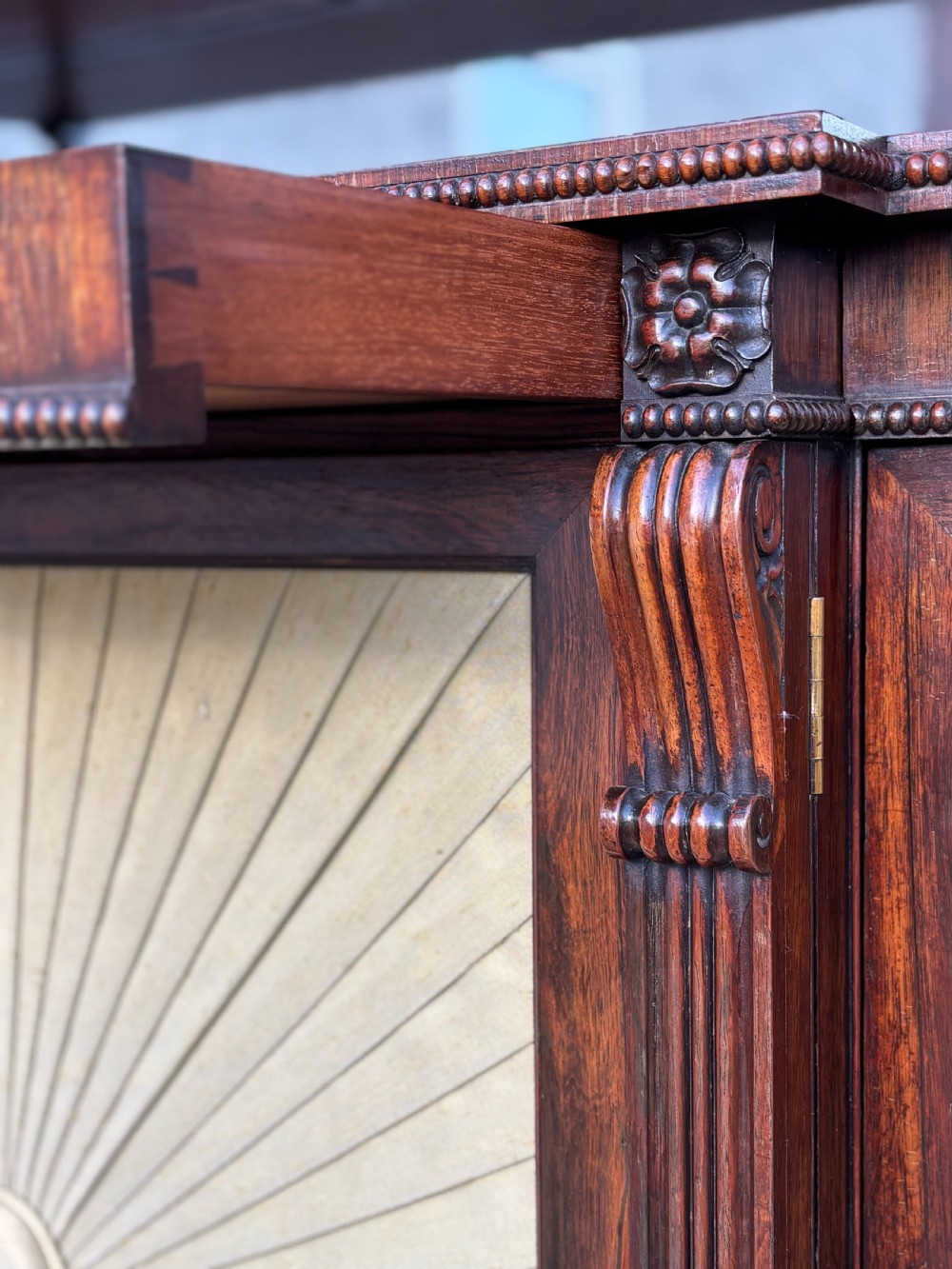 A Regency rosewood sideboard featuring three doors with sunburst pleated panels, a mirrored upper shelf supported by brass columns, and a pierced brass top gallery. View XI
