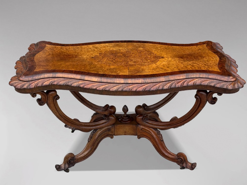 A 19th-century Victorian burr walnut centre table featuring a serpentine top with central floral marquetry and carved scroll legs on castors.