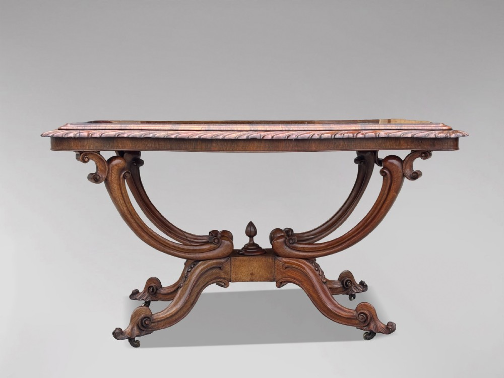 A 19th-century Victorian burr walnut centre table featuring a serpentine top with central floral marquetry and carved scroll legs on castors. View II