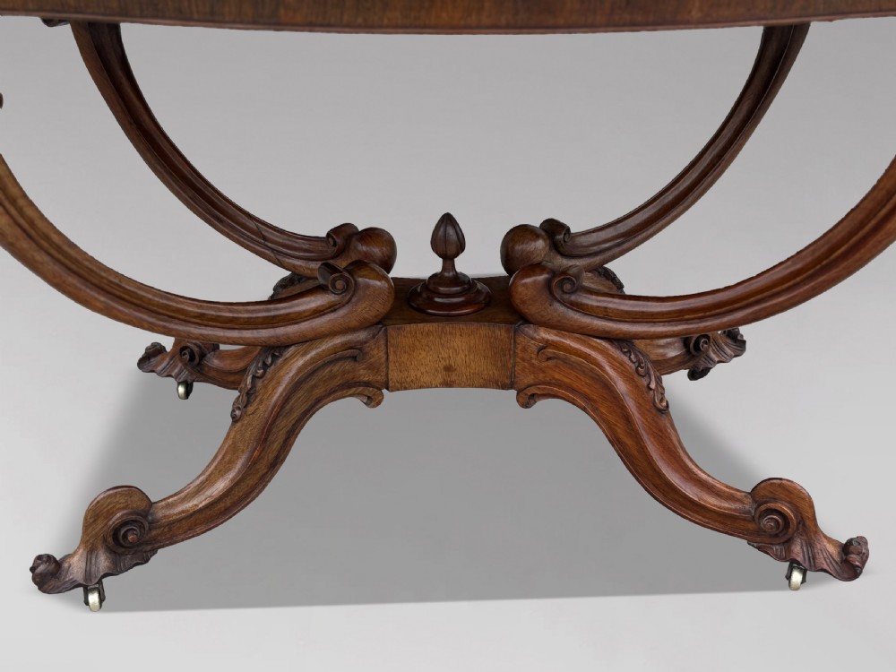 A 19th-century Victorian burr walnut centre table featuring a serpentine top with central floral marquetry and carved scroll legs on castors. View VI