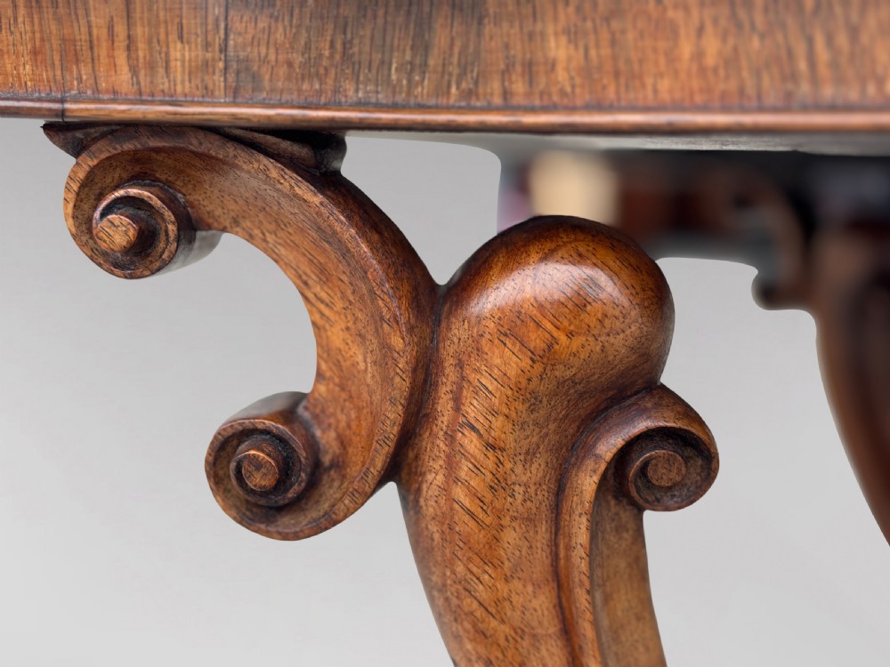 A 19th-century Victorian burr walnut centre table featuring a serpentine top with central floral marquetry and carved scroll legs on castors. View VII