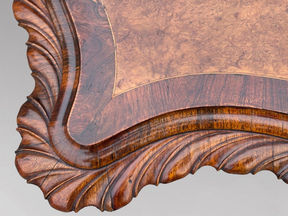 A 19th-century Victorian burr walnut centre table featuring a serpentine top with central floral marquetry and carved scroll legs on castors. View IX
