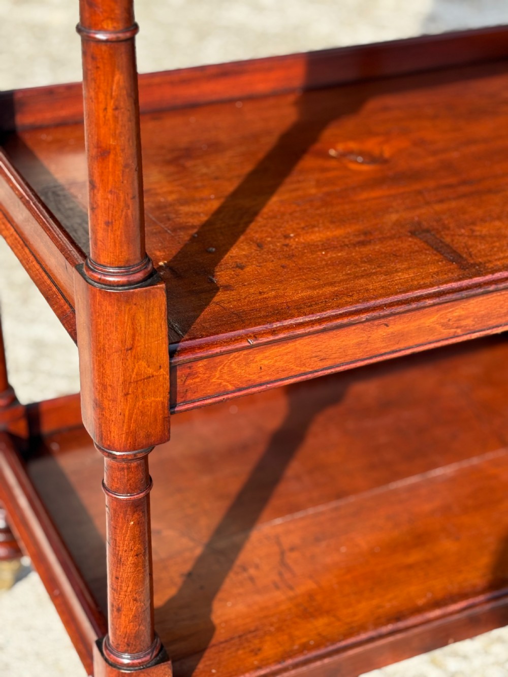 A four-tier George IV mahogany whatnot featuring a sloped top reading surface, turned wooden upright supports, and brass castors at the feet. View IV