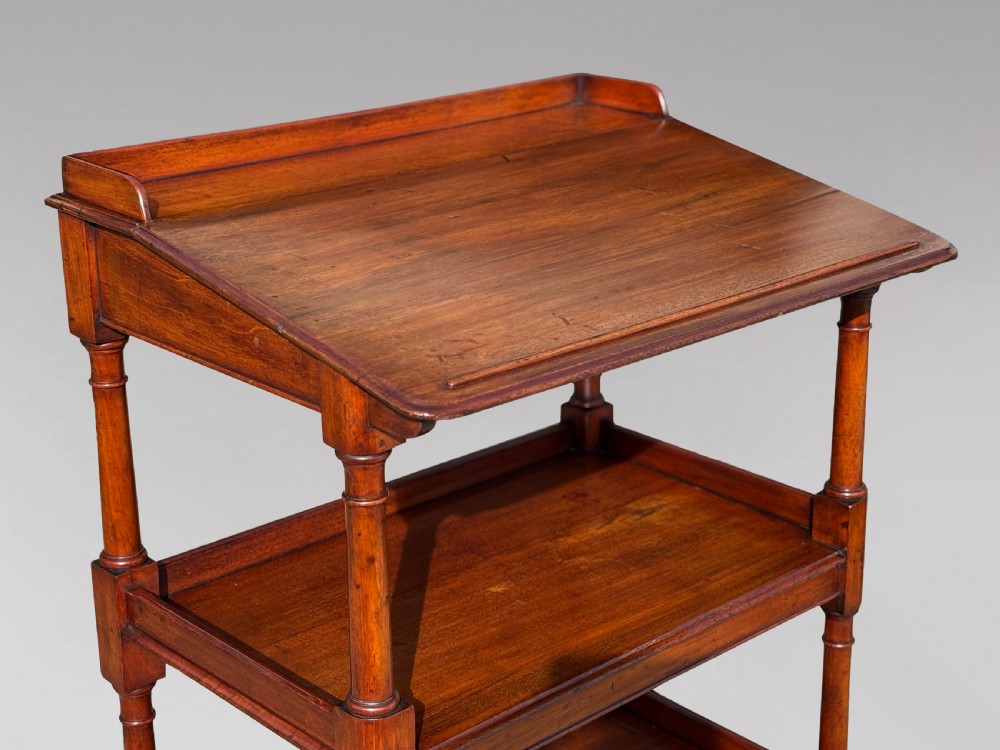 A four-tier George IV mahogany whatnot featuring a sloped top reading surface, turned wooden upright supports, and brass castors at the feet. View V