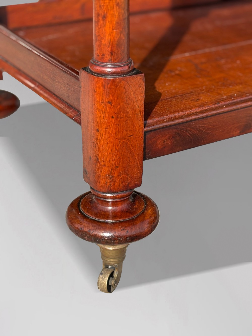 A four-tier George IV mahogany whatnot featuring a sloped top reading surface, turned wooden upright supports, and brass castors at the feet. View VI