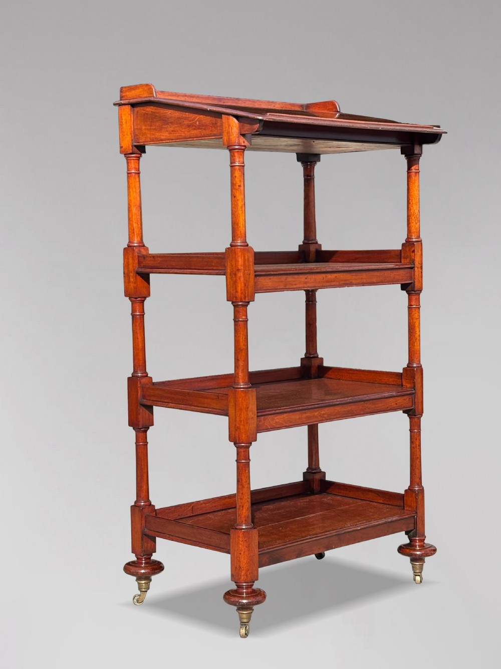 A four-tier George IV mahogany whatnot featuring a sloped top reading surface, turned wooden upright supports, and brass castors at the feet. View VII