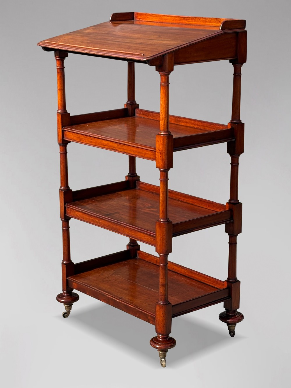 A four-tier George IV mahogany whatnot featuring a sloped top reading surface, turned wooden upright supports, and brass castors at the feet. View VIII