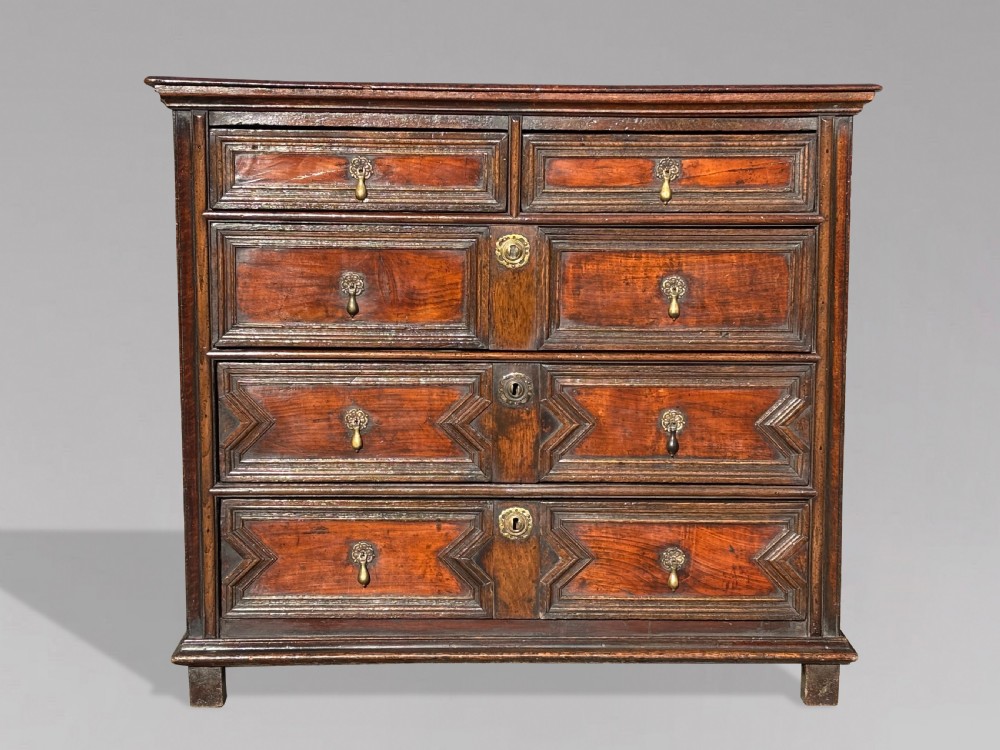 A 17th-century Charles II oak chest of drawers featuring geometric mitred mouldings, two short drawers over three long drawers, and brass teardrop handles.