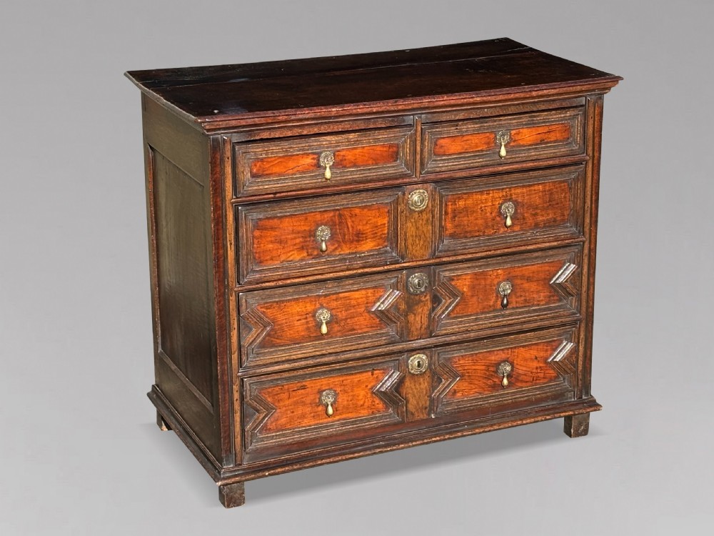A 17th-century Charles II oak chest of drawers featuring geometric mitred mouldings, two short drawers over three long drawers, and brass teardrop handles. View IV