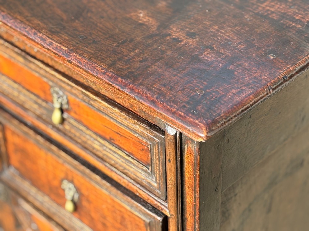 A 17th-century Charles II oak chest of drawers featuring geometric mitred mouldings, two short drawers over three long drawers, and brass teardrop handles. View IX